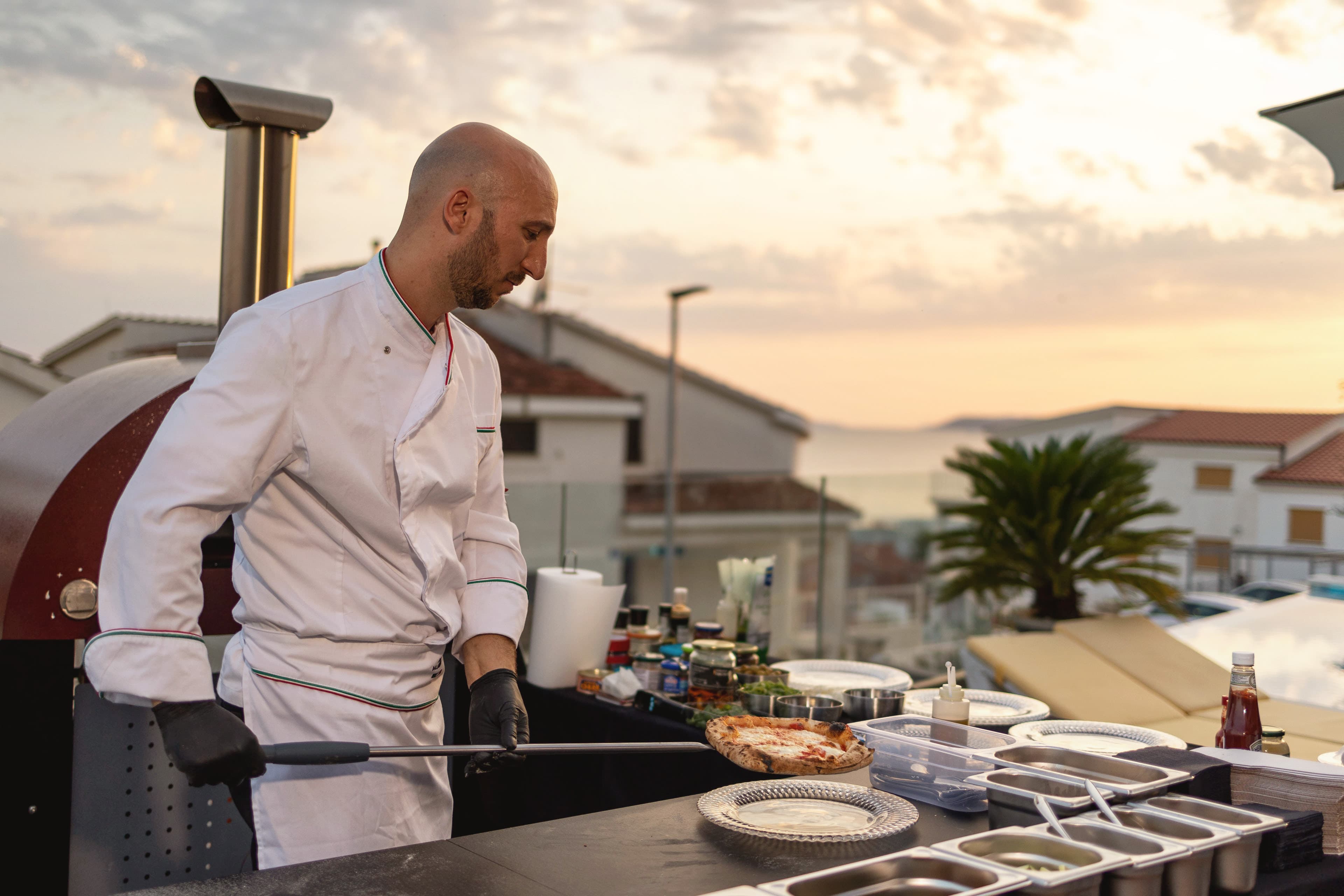 Chef cooking pizza at the rooftop wood-fired oven at sunset